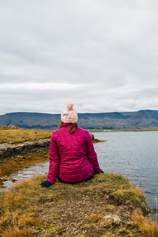 A white woman sits by a lake enjoying the natural scenery