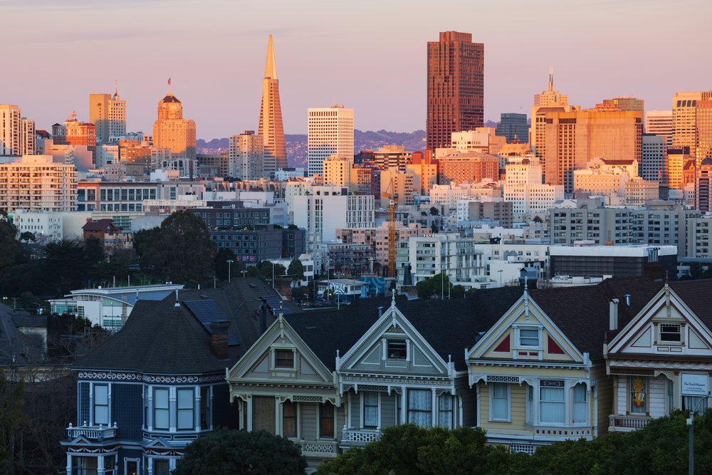 Sunset view of downtown San Francisco skyline behind Victorian painted ladies houses with warm light and city trees, Cityscapes, City Life, California, USA.