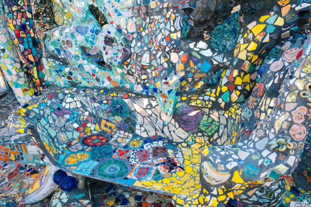 Colorful mosaic ceramic tiles cover an outdoor bench and surrounding art installation with sculptural shapes and textured surfaces, CA, USA.