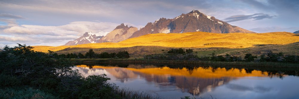 Los Cuernos mountain peaks reflect in a calm lake during sunrise, Torres del Paine National Park, Chile.