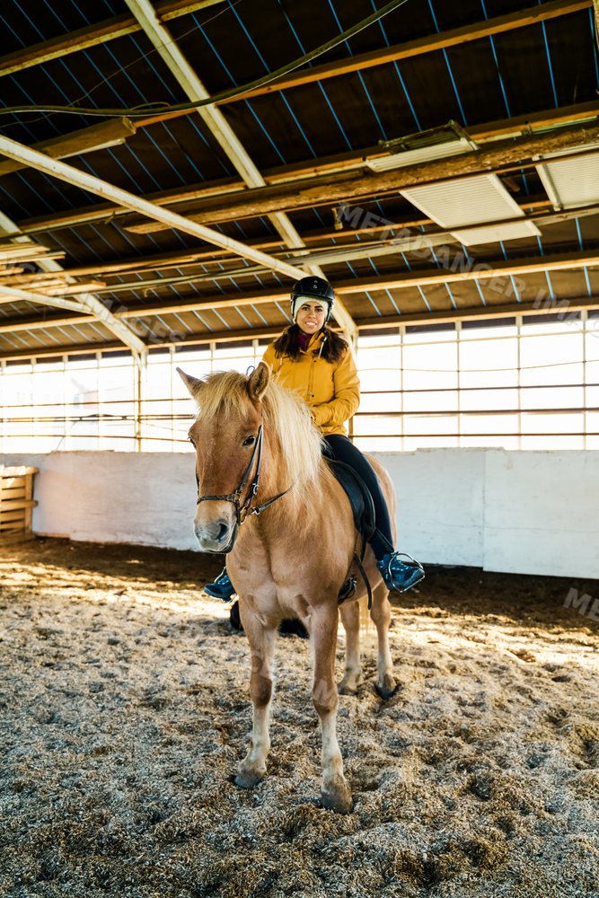A white woman rides a horse in an indoor riding arena