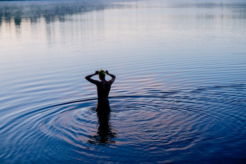 Woman stands in a lake at sunset putting on a swim cap, creating ripples in the calm water, USA.