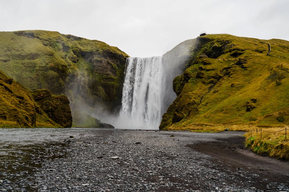 A powerful waterfall cascades down moss-covered cliffs into a rocky riverbed, Iceland.
