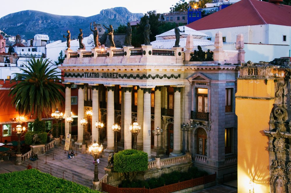 Teatro Juarez opera house with classical columns and statues illuminated at dusk, with mountains in the background, Guanajuato, Mexico.