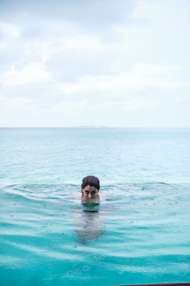 A white woman swimming in an infinity pool in the Maldives with ocean