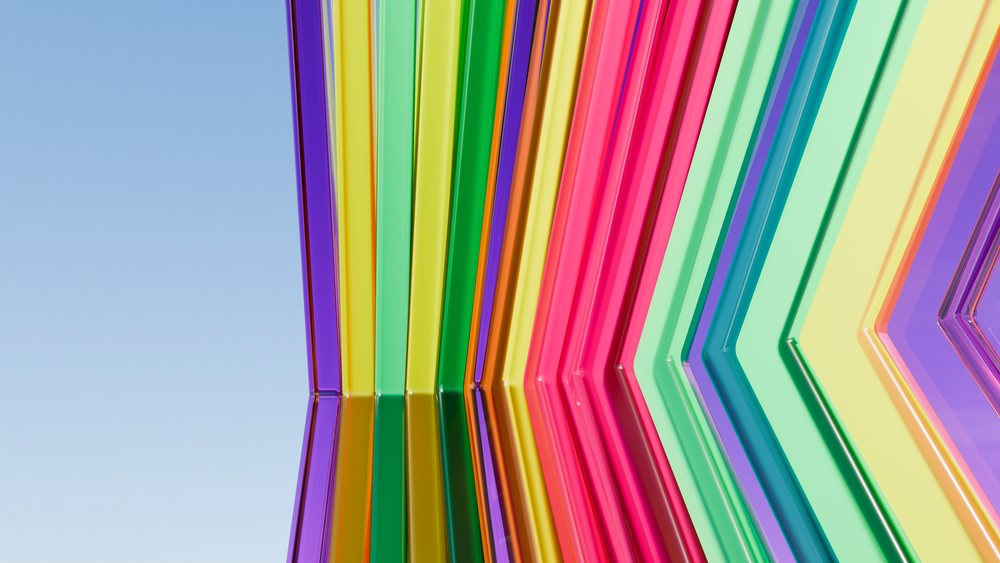 Colorful translucent plexiglass panels arranged in symmetrical geometric shapes with mirrored reflections against a clear blue sky.