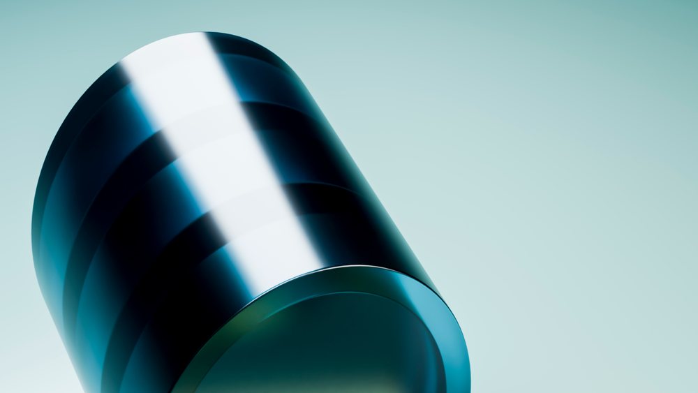 Shiny black metal cylinder with reflective polished surface on a light blue background in a studio setting.