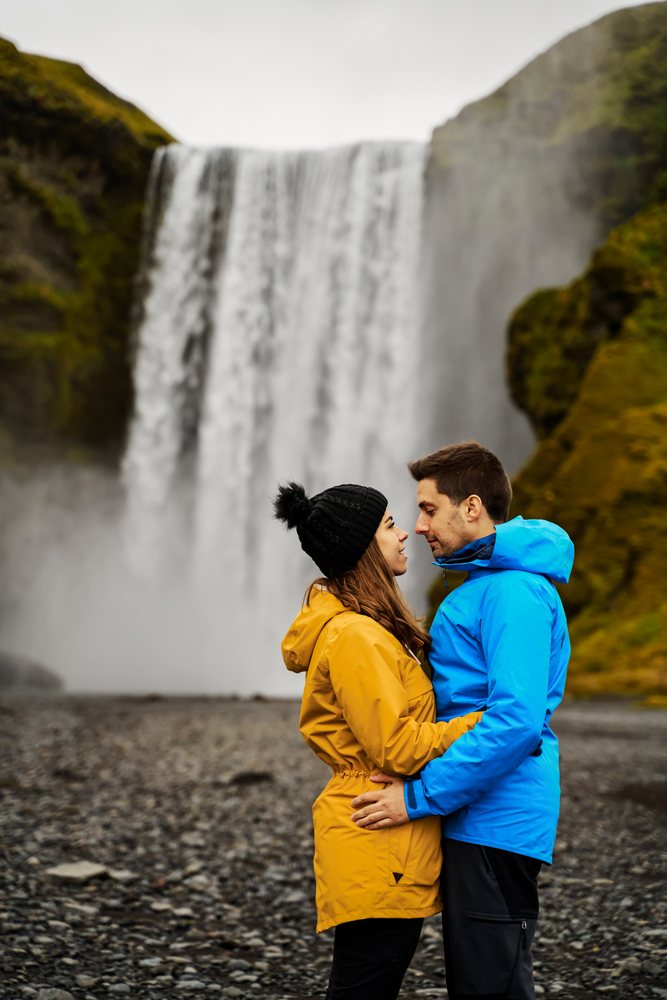 A couple embraces in colorful jackets near a waterfall, Iceland.