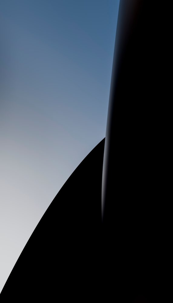 Sunlight illuminates a smooth aerodynamic airplane wingtip against a clear blue gradient sky during daytime flight.