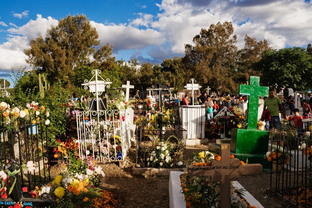 Day of the Dead cemetery, decorated with colorful crosses and marigold flowers with visitors present, San Miguel de Allende, Mexico.