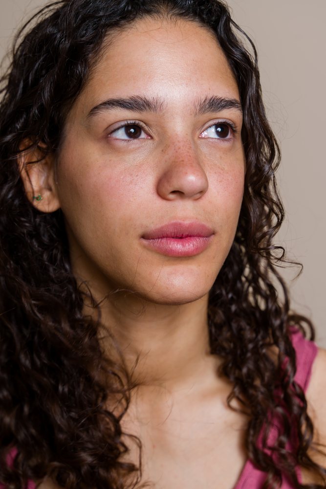 Woman with curly hair and freckles looking away in an indoor portrait beauty shoot, Spain.