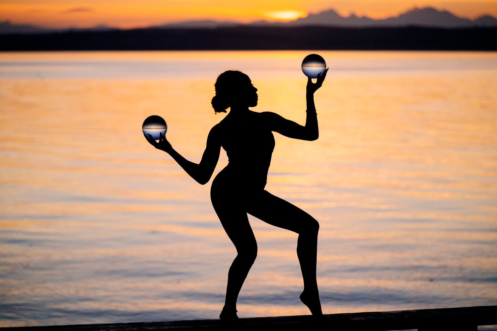 Silhouette of a woman balancing two glass balls in a yoga pose at sunset by the water, USA.