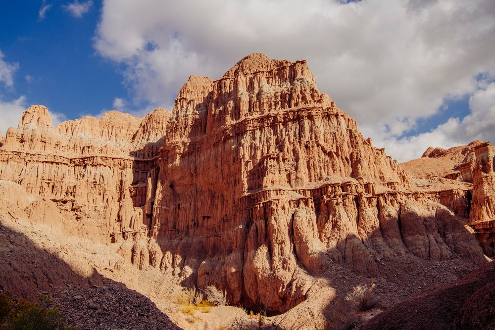 Sunlit sedimentary red rock formations and cliffs with deep erosion patterns at Cathedral Gorge State Park under a partly cloudy sky, Nevada, USA.