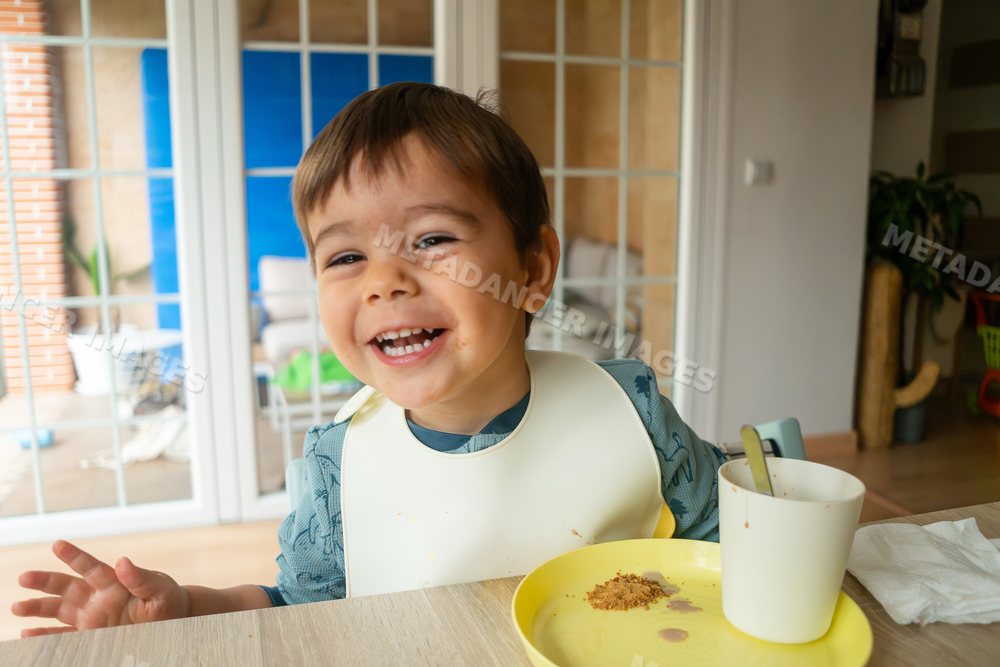 A toddler happily eating a snack indoors featuring a white model