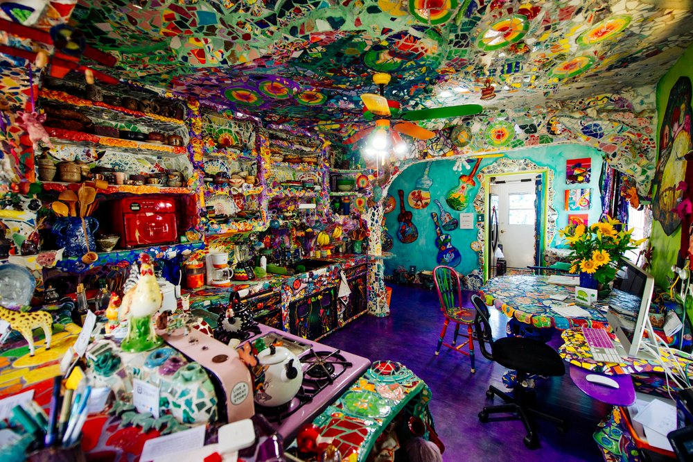 Eclectic colorful kitchen featuring mosaic tiles, painted ceiling, dining table with sunflowers, and a computer desk, CA, USA.