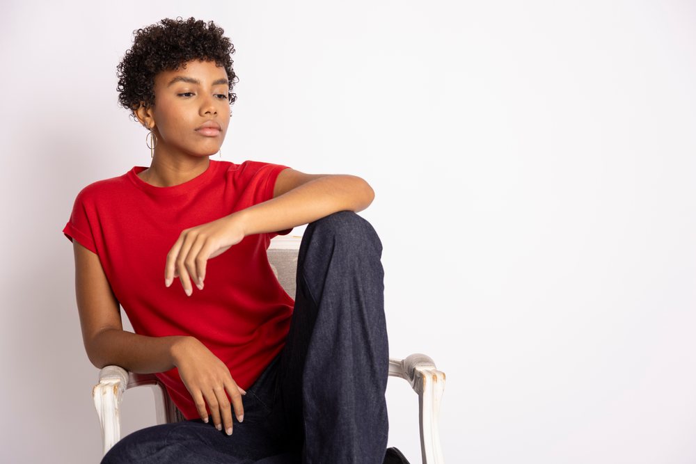 Woman wearing red shirt sitting thoughtfully in a chair against a white studio background, fashion, young culture.