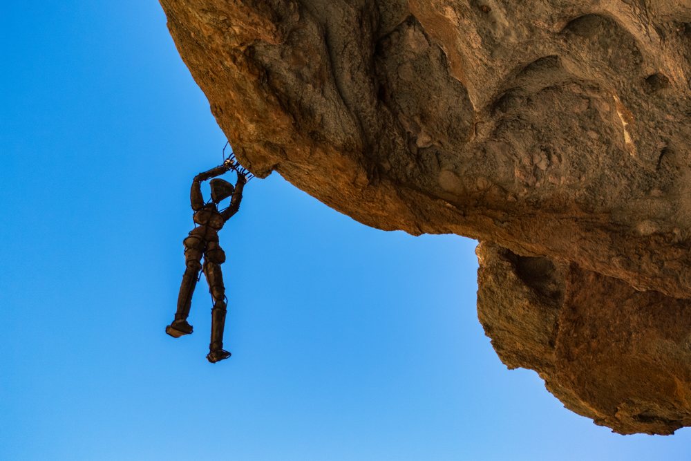 Metal sculpture of a human figure hanging from a cliff rock face against a clear blue sky, landscape, wildlife, Sesfontein, Kunene Region, Namibia.