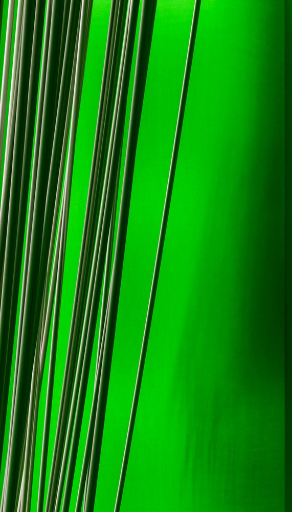 Closeup of thin vertical rods forming a striped pattern against a bright green background in an abstract minimalist composition.