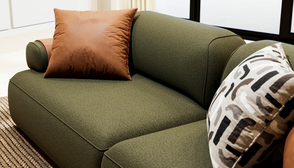 Green fabric sofa with brown leather and patterned textile cushions in a modern indoor living room near a window.