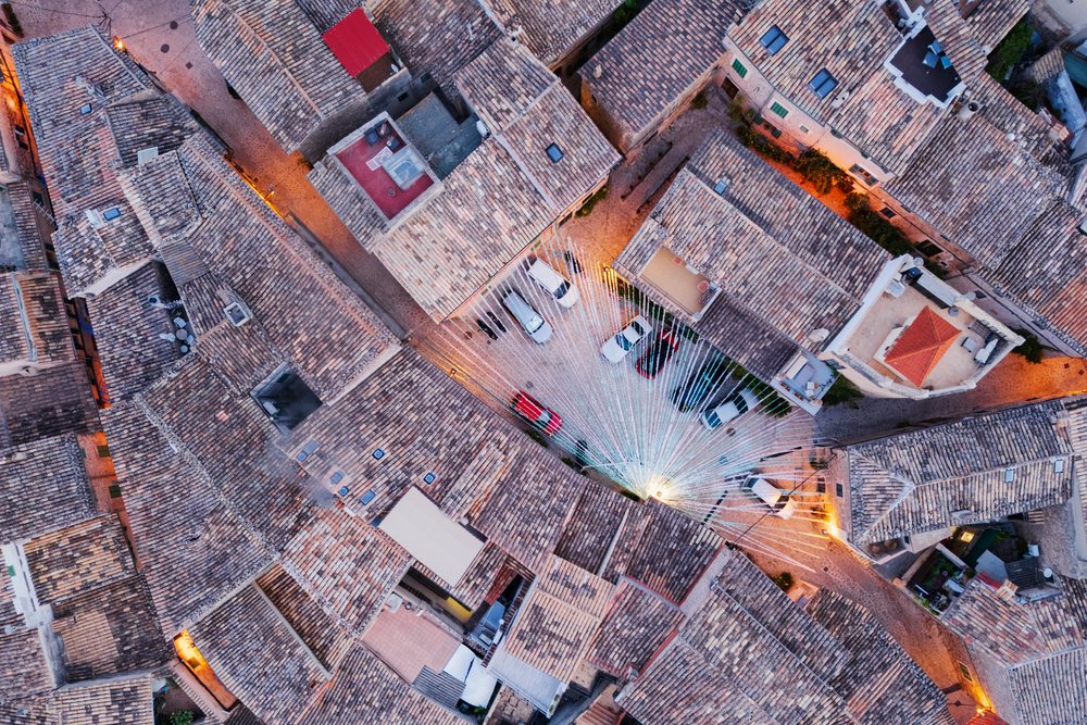 Aerial view of Valdemossa village rooftops with terracotta tiles, paved streets, and string lights over a parking lot at Dawn, Landscape, Lifestyle, Mallorca, Spain.