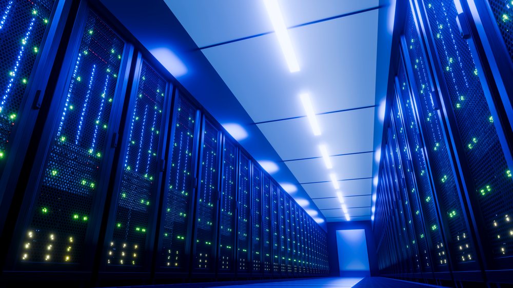 Multiple computer server racks illuminated by blue lighting in a modern data center server room hallway.
