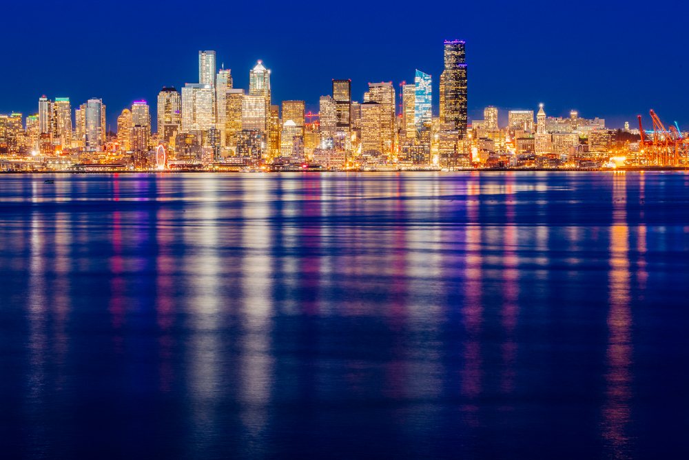 Seattle city skyline glowing with lights reflected in calm water at night under a clear sky, USA.