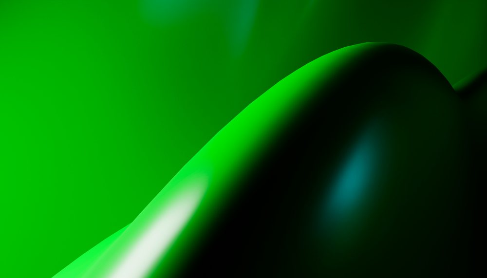 Close-up of a smooth, shiny green surface with curved abstract shapes under studio lighting.
