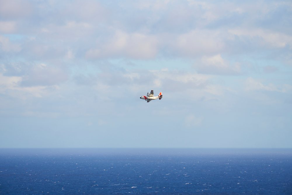 Airplane flies above the ocean under a partly cloudy sky with a distant horizon visible, Oahu, Hawaii, USA.