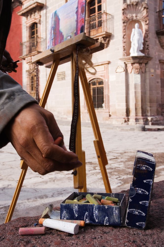 Artist's hand working with chalk pastels on a wooden easel outside a historic building, San Miguel de Allende, Mexico.