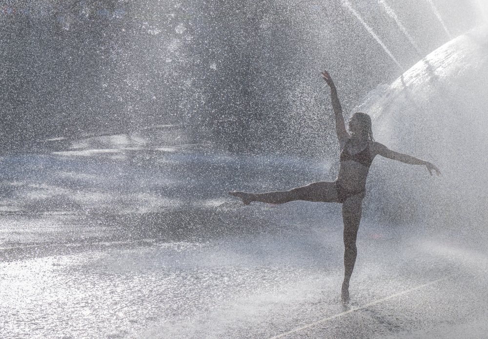 Woman performing a ballet pose amid the spray of an outdoor water fountain, partner, acrobatics, yoga, USA.