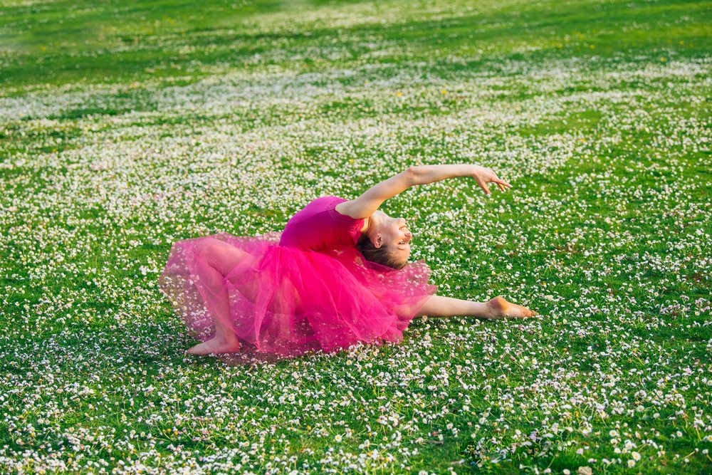 Ballet dancer in a pink tutu gracefully poses outdoors on a green grass field sprinkled with white flowers, USA.