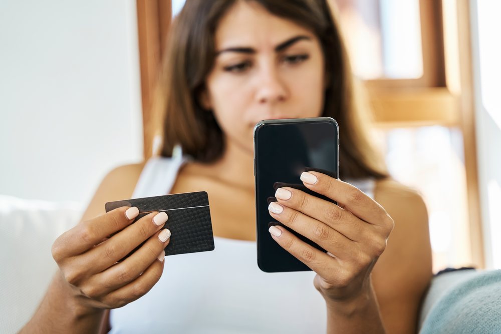 A young white woman uses her smartphone and credit card for online