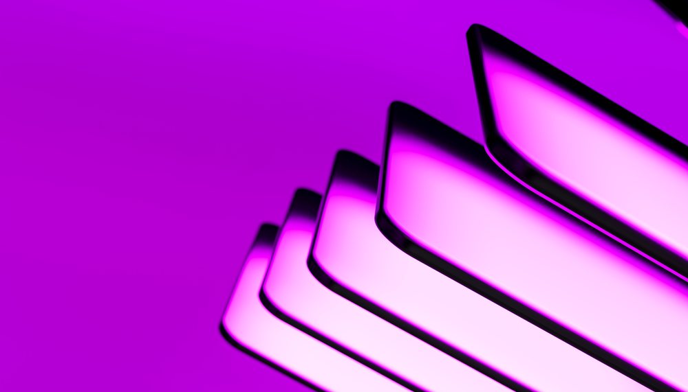 Stack of modern mobile phones with glowing purple screens against a purple background.