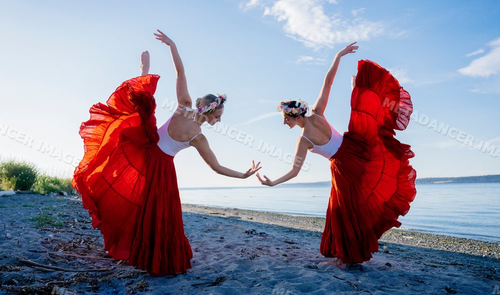 Two white women perform partner yoga acrobatics on a beach in WA, USA