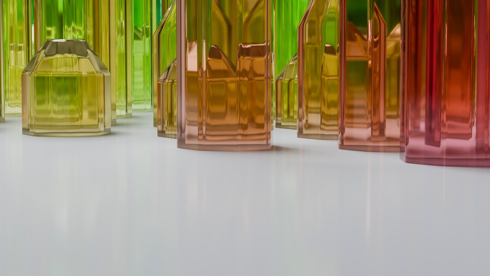 Colored glass bottles in green, yellow, orange, and red hues are arranged on a reflective white table surface in a studio-lit still life composition.