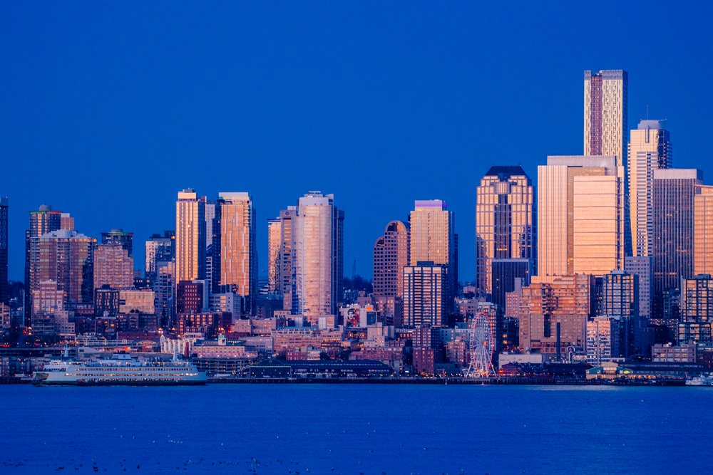 Seattle city skyline with waterfront ferry and Great Wheel illuminated at dusk, USA.