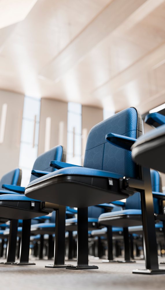 Blue molded plastic chairs with armrests arranged in rows inside a well-lit auditorium or conference hall.