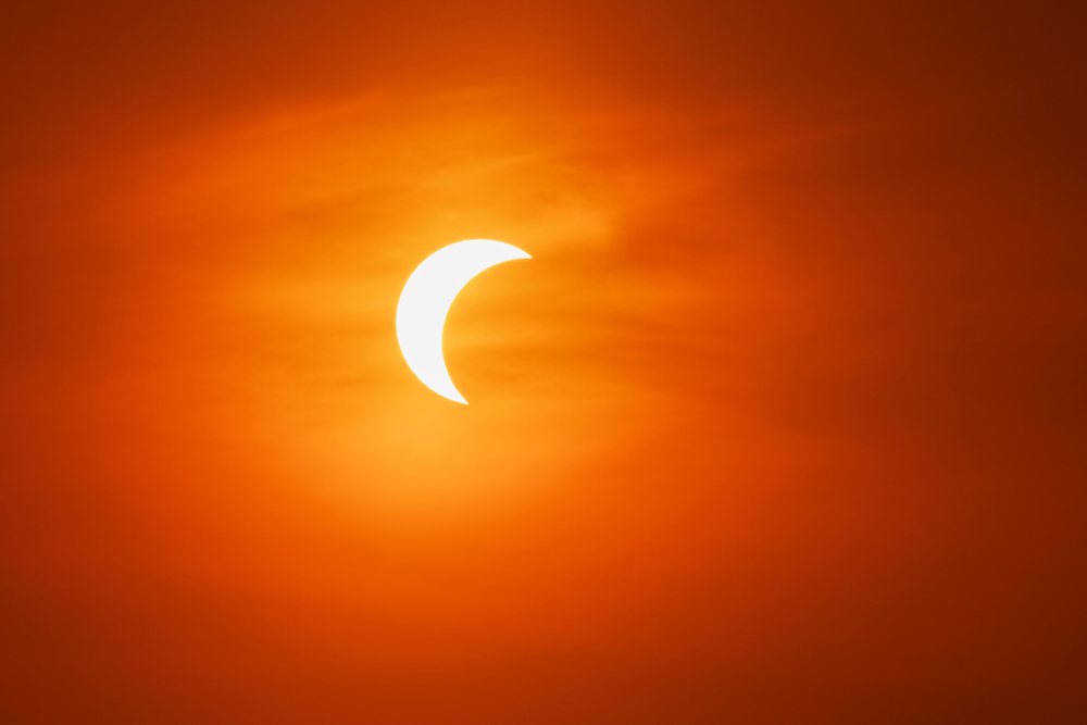 Partial solar eclipse visible over Valldemossa, with the sun partially obscured by the moon against an orange sky, Landscape, Lifestyle, Mallorca, Spain.