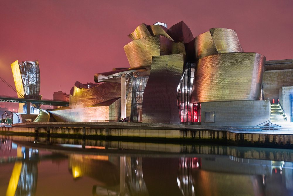 Guggenheim Museum Bilbao is illuminated at night with its reflection on the river, Spain.