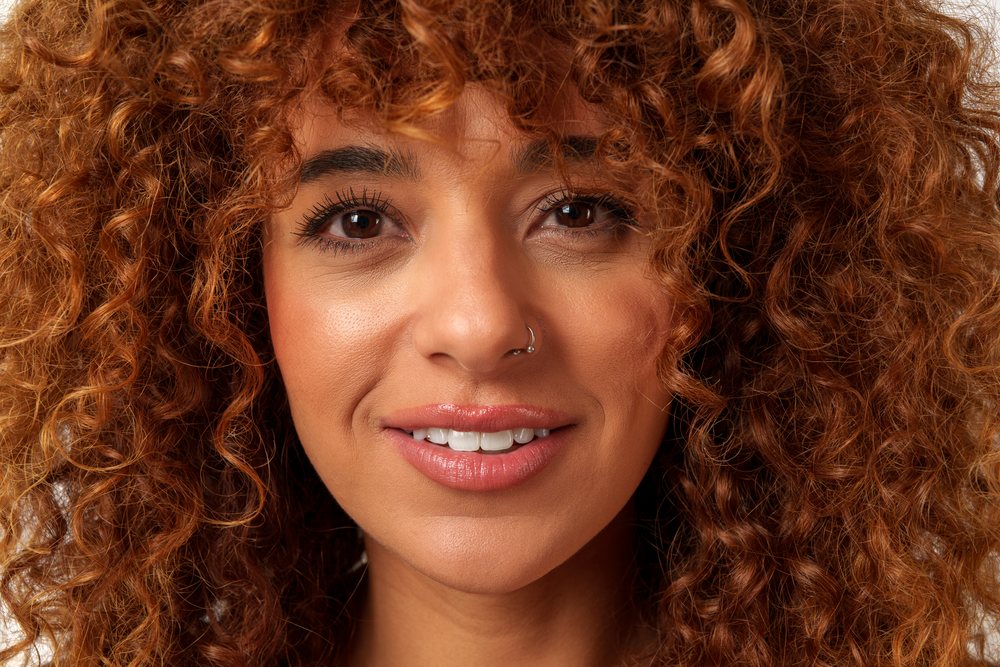 Woman with curly red hair and a nose ring smiling in a portrait at a studio, Malaga, Spain.