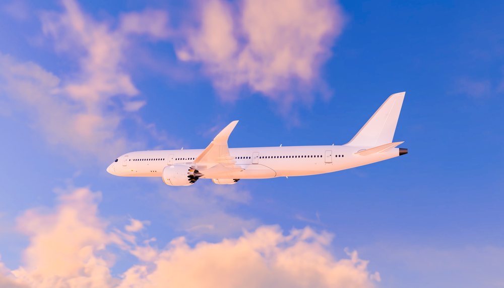 A white commercial airplane flies through a blue sky with pink-tinged clouds during sunset, travel, fly, vacation.