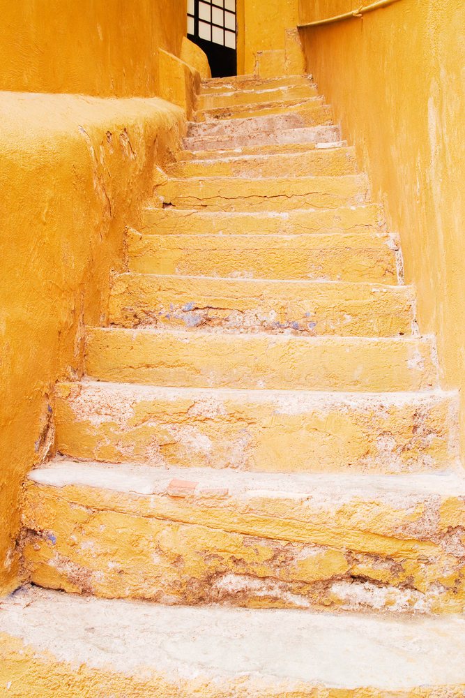 Yellow weathered stone steps with textured walls on both sides lead up to an open doorway, Guanajuato, Mexico.
