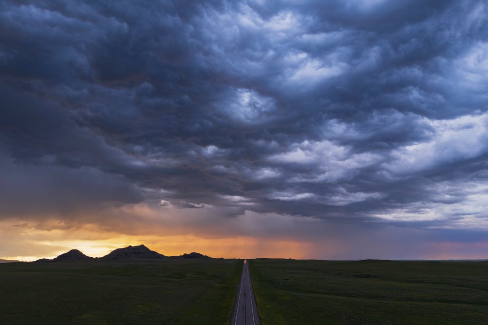 Sunset over Crow Buttes with dark storm clouds and a highway stretching through open grassland, Storm Chasing, Weather, Environmental, Redig, South Dakota, USA.