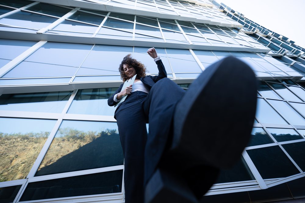 Businesswoman wearing a black suit steps forward in front of a modern glass office building, business trip, Spain, Santiago De Compostela.