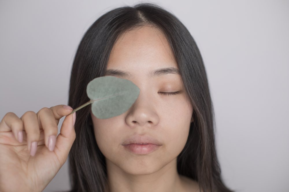 Close-up portrait of a serene woman with closed eyes holding a leaf over one eye, Art, emotional.