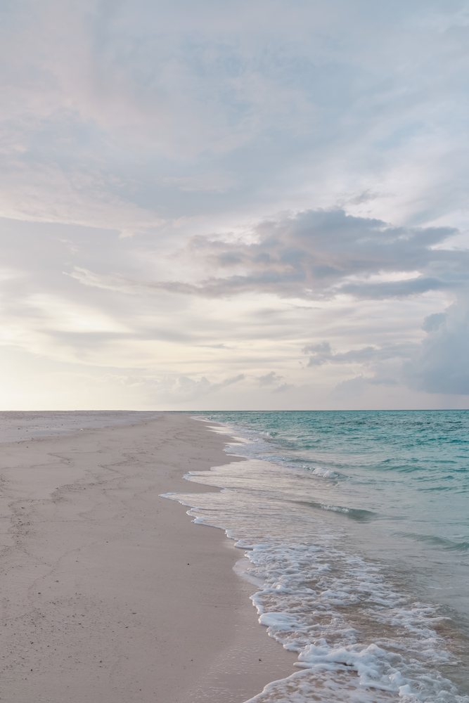 A tranquil beach shoreline with gentle waves under a cloudy sky in the, Maldives.