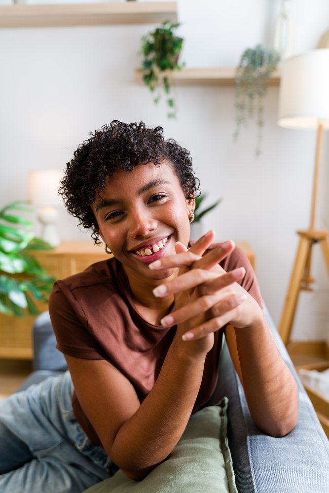 Smiling woman with curly hair sits on a couch in a cozy indoor living room setting, Spain.
