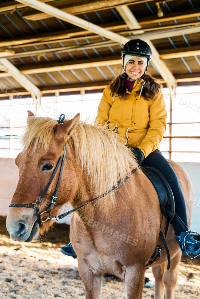 A white woman rides a horse inside an indoor arena