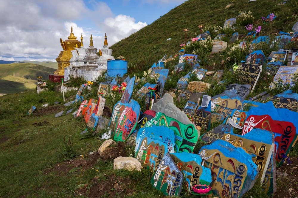 Colorful painted Mani Stones are arranged on a hillside near a golden stupa and smaller white stupas, Kham Tibet, China, Tagong, Sichuan Province, People's Republic of China.