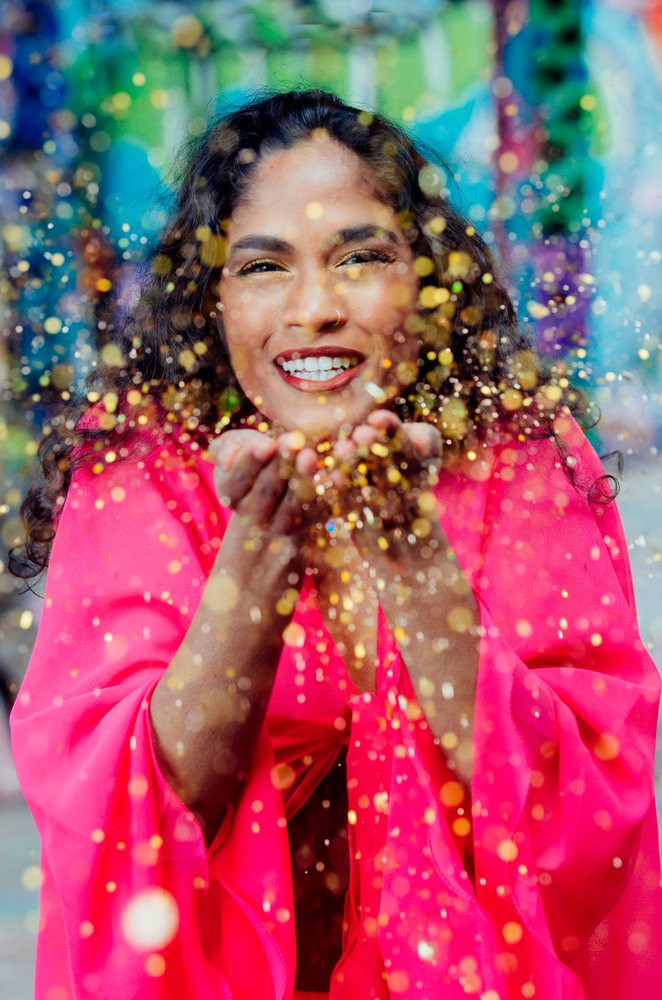 Woman wearing bright pink garment blowing colorful glitter during a festive celebration outdoors, USA.